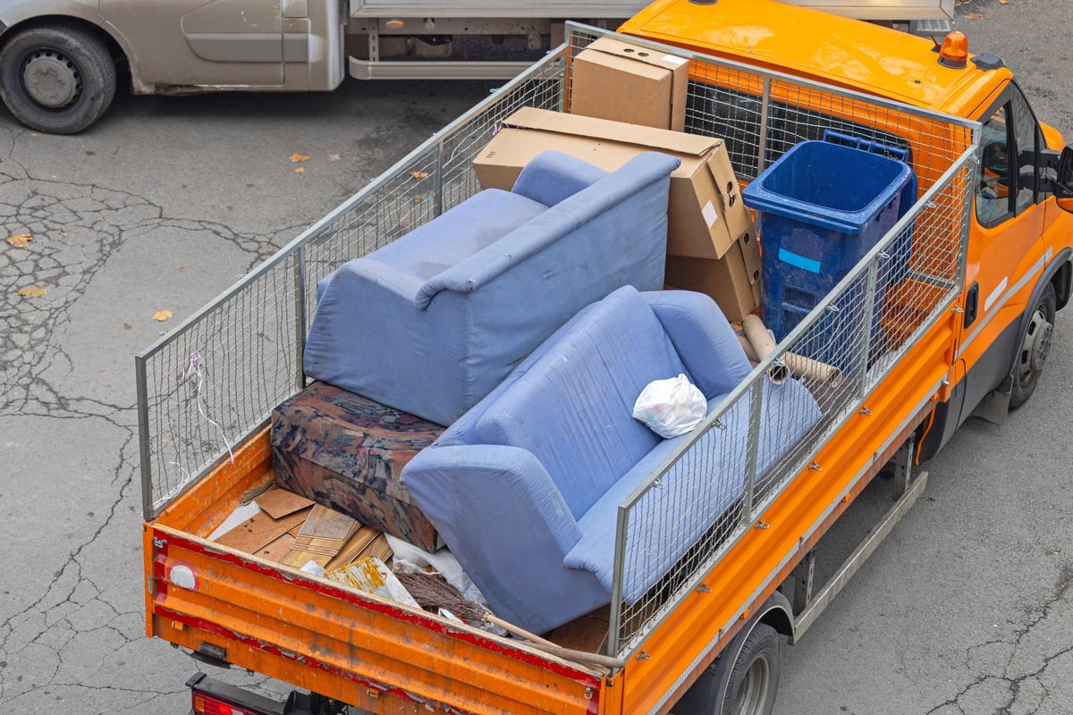 A pile of discarded furniture including a sofa, chair, and various cushions on a city sidewalk, highlighting urban waste and the need for proper disposal or recycling